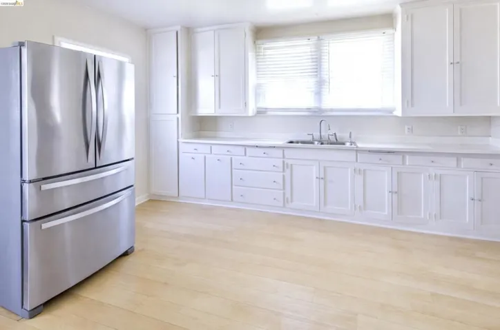 Kitchen with freestanding refrigerator, light countertops, white cabinetry, and light wood-style flooring