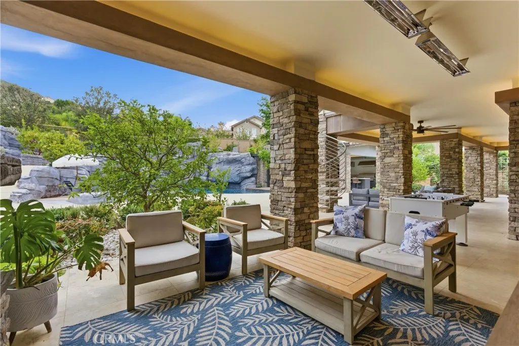 Covered outdoor seating area with spiral staircase leading to second level balcony and pool views