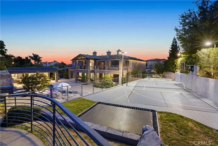 Angled aerial view highlighting the resort-style backyard, outdoor kitchen area, pool, and sports court.