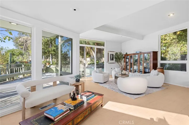 The main level is designed for both relaxed living and effortless entertaining, featuring a dramatic living room with vaulted ceilings, a statement fireplace that anchors the room, and glass doors that open to a wraparound deck framed by greenery and ocean views, extending to a spacious yard.