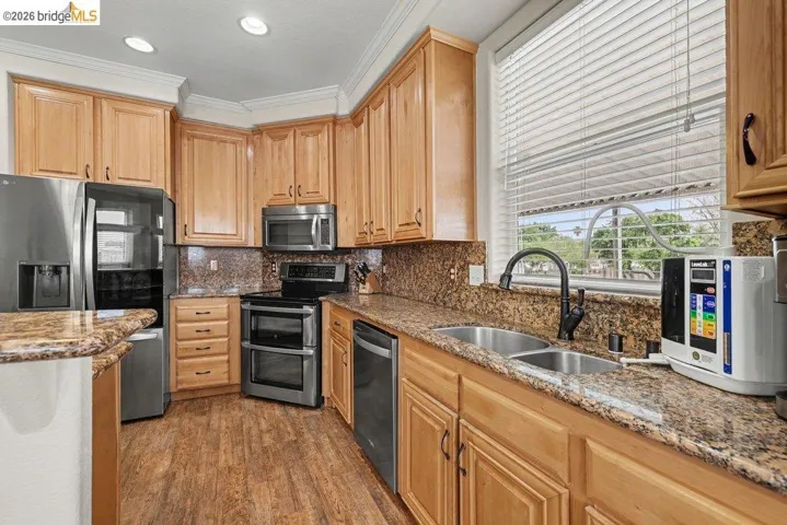 Kitchen with stainless steel appliances, light stone countertops, dark wood finished floors, tasteful backsplash, and ornamental molding