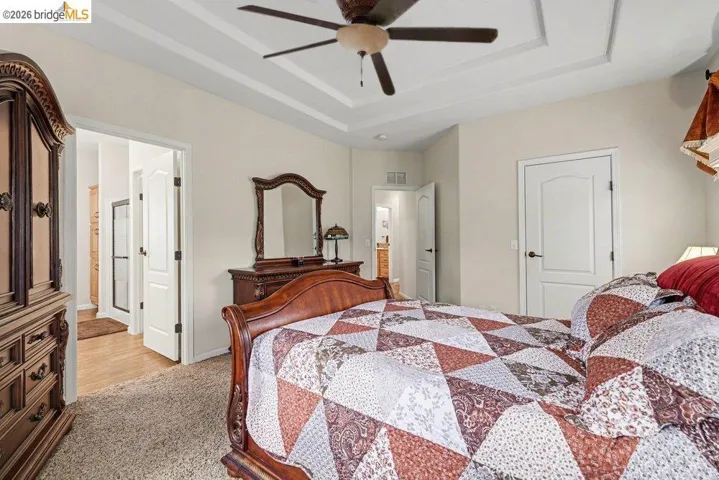 Carpeted bedroom featuring ceiling fan and a tray ceiling