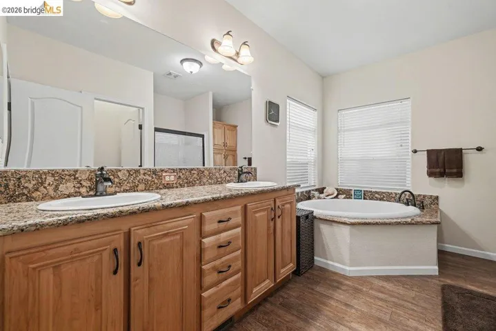 Full bath featuring double vanity, a bath, dark wood finished floors, and a shower stall