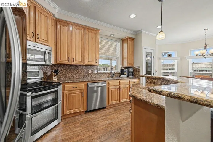 Kitchen featuring ornamental molding, stainless steel appliances, dark stone counters, dark wood finished floors, and tasteful backsplash