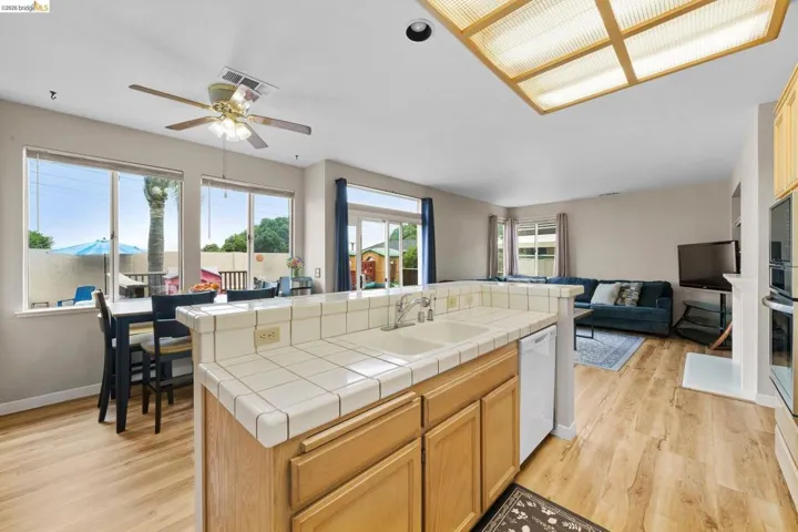 Kitchen with open floor plan, a kitchen island with sink, tile counters, a ceiling fan, and light wood-type flooring