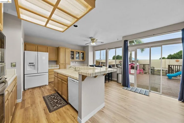 Kitchen featuring tile countertops, white appliances, an island with sink, glass insert cabinets, and light wood-style flooring