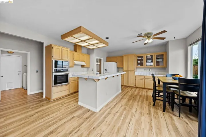 Kitchen featuring a kitchen bar, tile countertops, light wood finish cabinetry, stainless steel oven, and a kitchen island