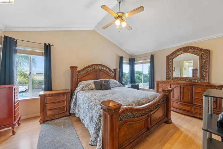 Bedroom featuring light wood-style floors, ornamental molding, lofted ceiling, and a ceiling fan