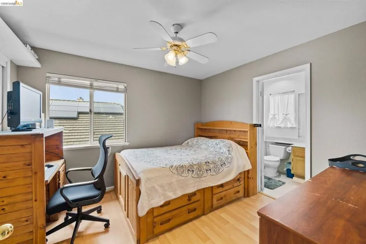 Bedroom with a desk, light wood-style flooring, ceiling fan, and connected bathroom