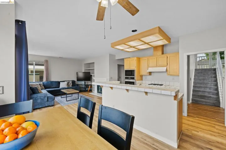 Kitchen with light wood finish cabinets, a breakfast bar area, light wood-style flooring, tile counters, and a ceiling fan