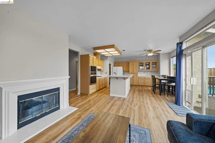 Living area featuring light wood-style flooring, a ceiling fan, and a glass covered fireplace