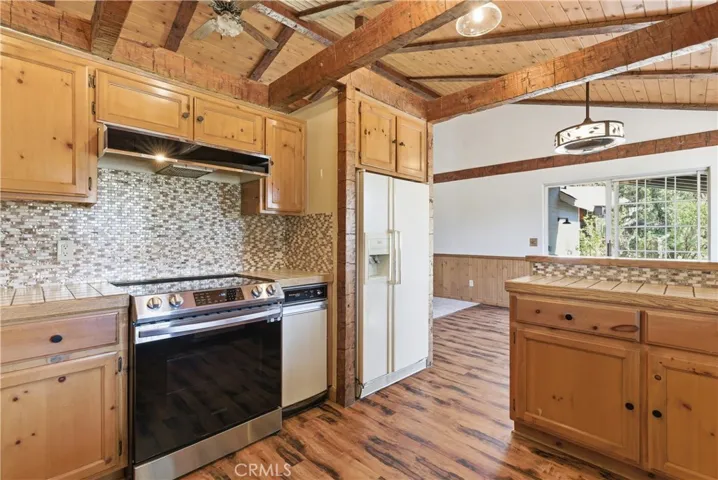 Kitchen with backsplash tile, stove, trash compactor, and fridge.  Appliances included! Opens up to eating area near windows that bring in natural light.