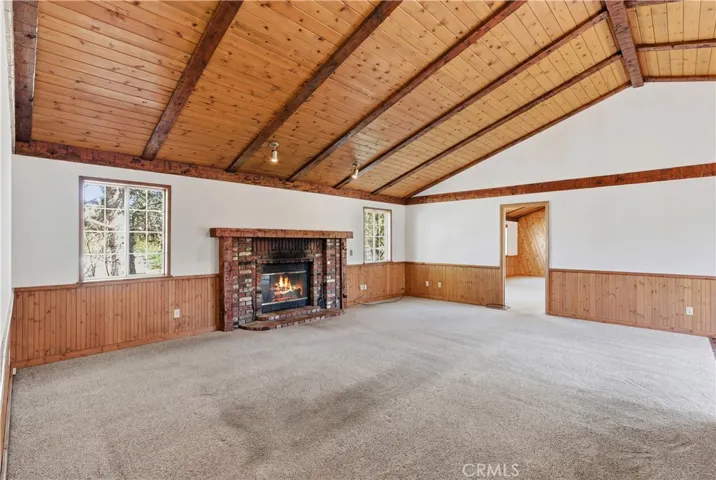 Living Room boasts beamed vaulted ceiling, wainscoting, and cozy brick fireplace.