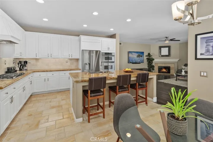 Chef's kitchen with granite slab counter tops, tile backsplash, center island with stainless steel farm sink & dining counter, dual oven/microwave combo, warming drawer, 5 burner cook top, dishwasher, upgraded cabinetry with under counter lighting & spacious dining area