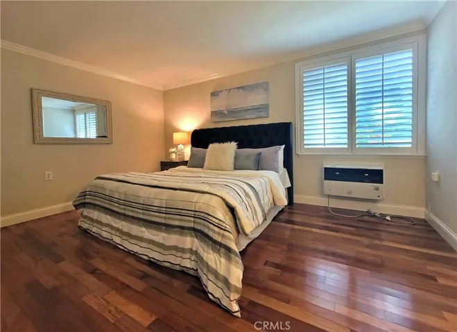 Primary bedroom with wood floors and AC wall unit.