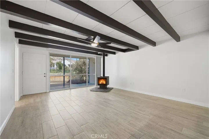 Large living room w beamed ceiling, wood burning stove, all new tile plank flooring and floor to ceiling window looking out to front yard and community green belt