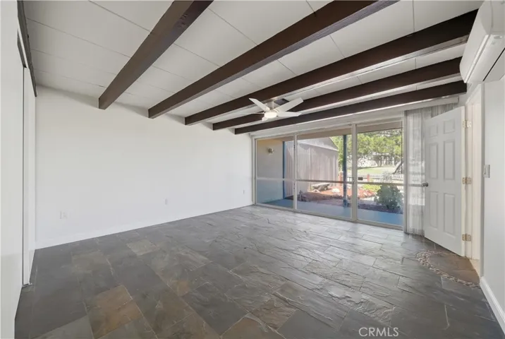 Front bedroom freshly painted w slate flooring, floor to ceiling windows looking out to front yard and community greenbelt w beamed ceiling and new ceiling fan/light fixture.