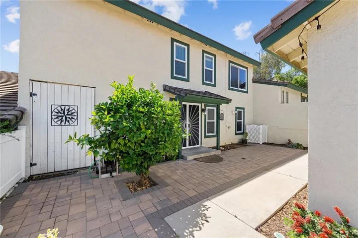 Gated front courtyard features paver hardscape, a covered entry, and a welcoming approach with mature greenery.