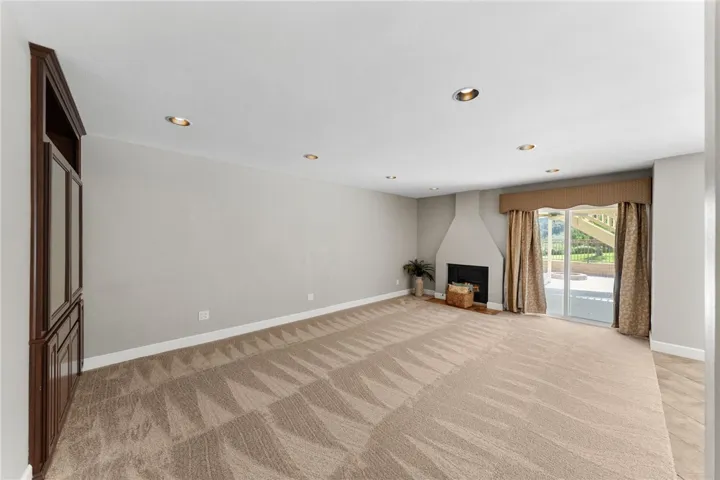 Spacious living room features plush carpeting, recessed lighting, a fireplace, and sliding glass doors that open to the backyard patio.