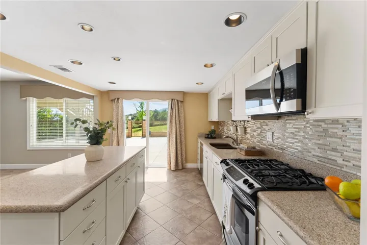 Bright kitchen layout includes a center island, gas range, and sliding glass door opening to the backyard patio and views beyond.