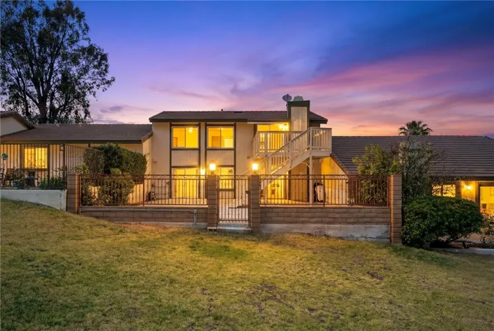 Evening rear exterior showcases the illuminated patio and deck area against a colorful sunset backdrop and scenic hillside surroundings.