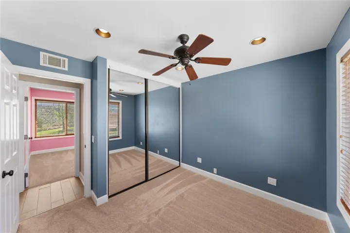 Comfortable secondary bedroom features mirrored closet doors, a ceiling fan, and soft natural light.