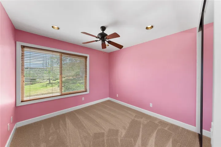 Cheerful bedroom with a large picture window, ceiling fan, and mirrored closet for added storage.