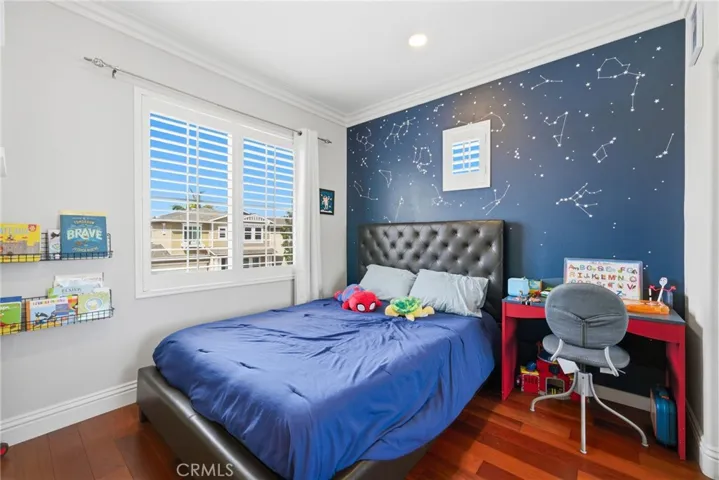 Secondary bedroom with hardwood flooring, ceiling fan, and natural light.