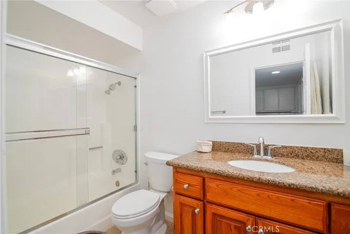 Hallway bath features warm wood vanity with granite countertop, tub/shower combo.