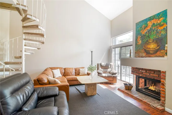 Enter into the living room featuring a soaring vaulted ceiling, fireplace, slider to the balcony and circular staircase to the loft.