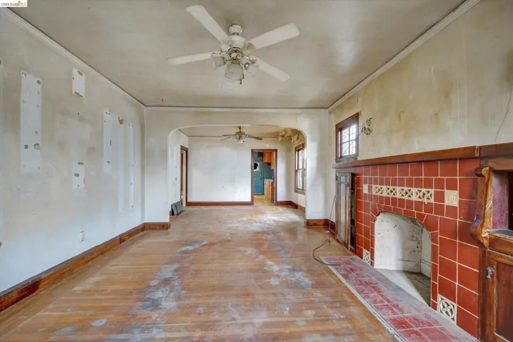 Unfurnished living room featuring a fireplace, hardwood / wood-style floors, a ceiling fan, arched walkways, and ornamental molding