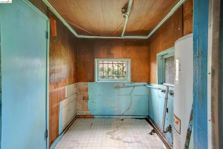 Laundry room with tile patterned floors, wooden ceiling, wooden walls, water heater, and crown molding