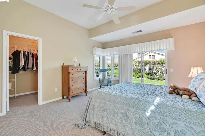 Bedroom with a walk in closet, light colored carpet, access to exterior, and ceiling fan