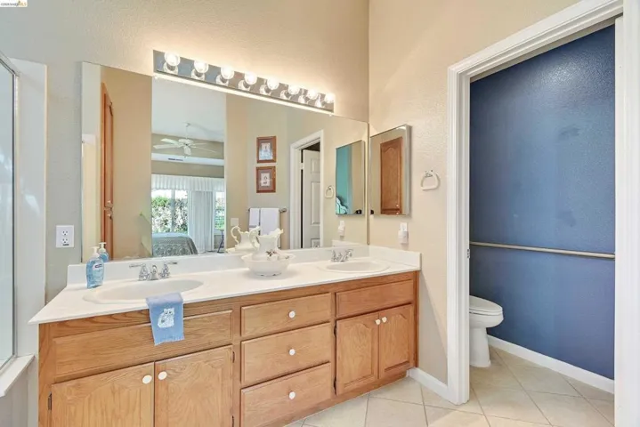 Ensuite bathroom featuring double vanity, light tile patterned flooring, a shower with door, and a ceiling fan