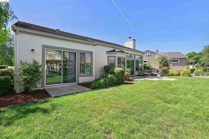 Rear view of property with stucco siding, a yard, a patio area, and a chimney
