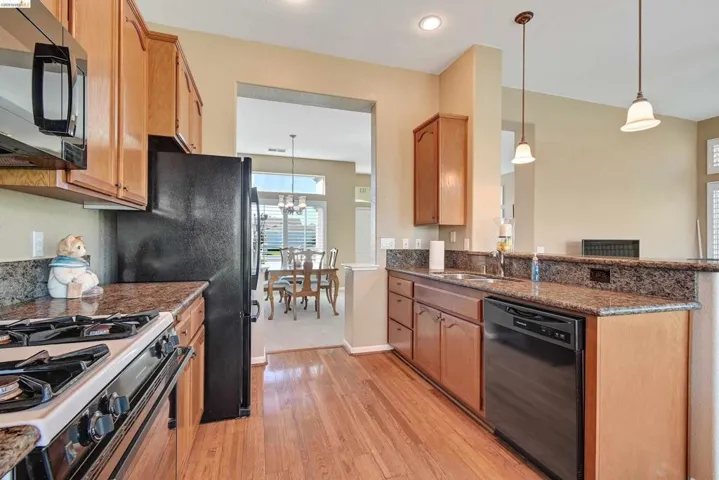 Kitchen with dark stone counters, hanging light fixtures, and black appliances