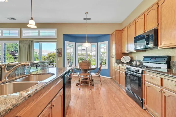 Kitchen featuring black appliances, dark stone counters, hanging light fixtures, and light wood-style flooring