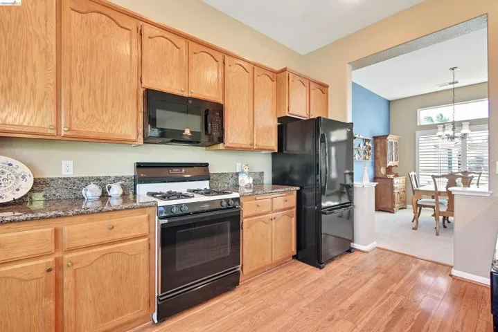 Kitchen with black appliances, dark stone counters, light wood-style floors, hanging lights, and light wood finish cabinetry