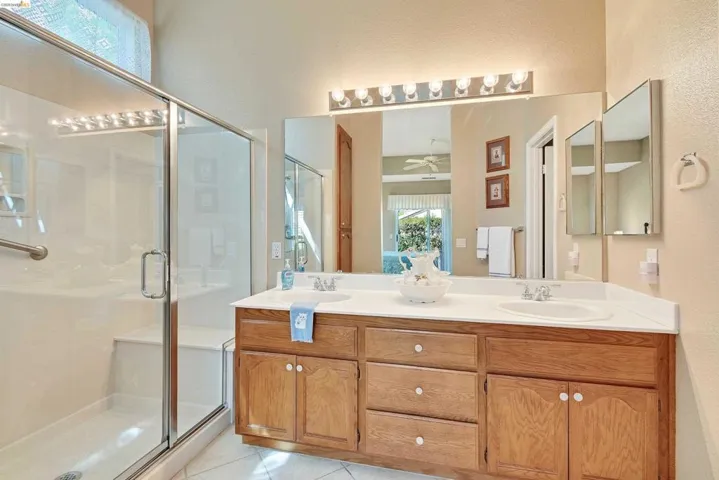 Full bath with double vanity, a stall shower, light tile patterned flooring, and a ceiling fan