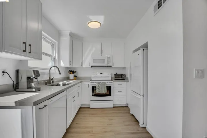 Kitchen with white appliances, white cabinetry, light wood-type flooring, and light countertops