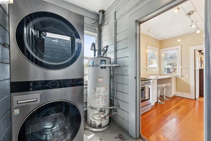 Laundry room featuring healthy amount of natural light, secured water heater, stacked washer / dryer, and rail lighting