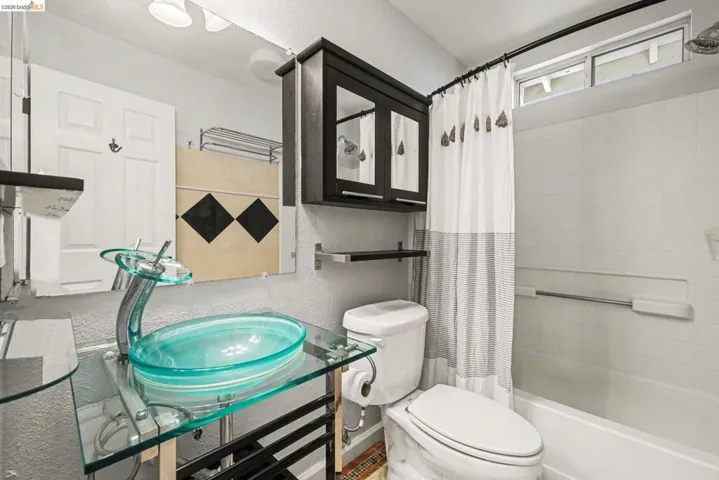 Bathroom featuring shower / bath combo, a textured wall, and vanity
