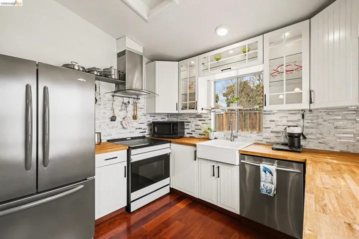 Kitchen with stainless steel appliances, wood counters, white cabinets, glass fronted cabinets, and recessed lighting