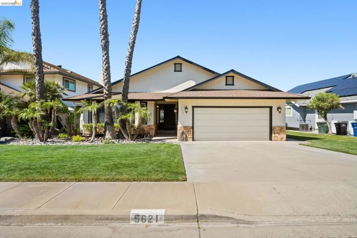 View of front of home with an attached garage, concrete driveway, a front lawn, stone siding, and a shingled roof
