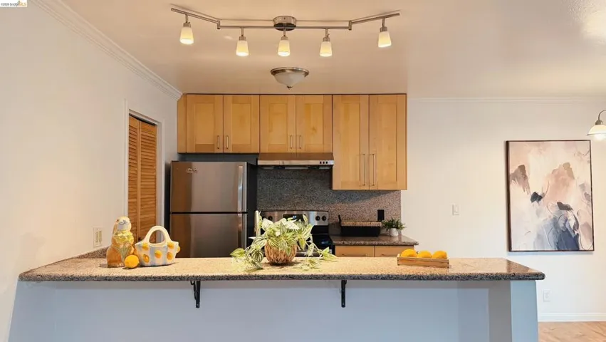 Kitchen with stainless steel appliances, a peninsula, backsplash, light wood finish cabinets, and light stone counters