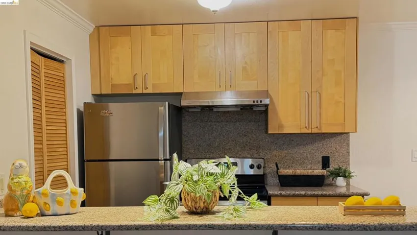 Kitchen with stainless steel appliances, light wood finish cabinetry, light stone counters, decorative backsplash, and crown molding