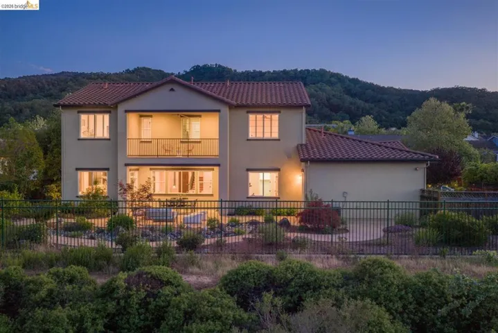 Back of house at dusk with a balcony, a fenced backyard, stucco siding, and a tile roof