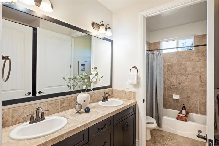 Full bathroom featuring double vanity, shower / bathtub combination with curtain, and light tile patterned floors