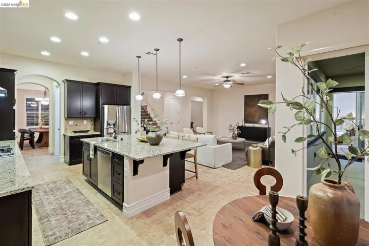 Kitchen with arched walkways, open floor plan, light stone counters, and a center island with sink