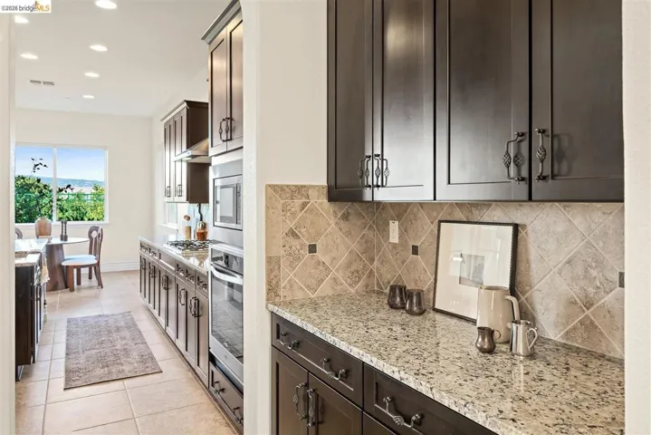 Kitchen with dark wood finish cabinets, light stone countertops, recessed lighting, light tile patterned flooring, and stainless steel appliances